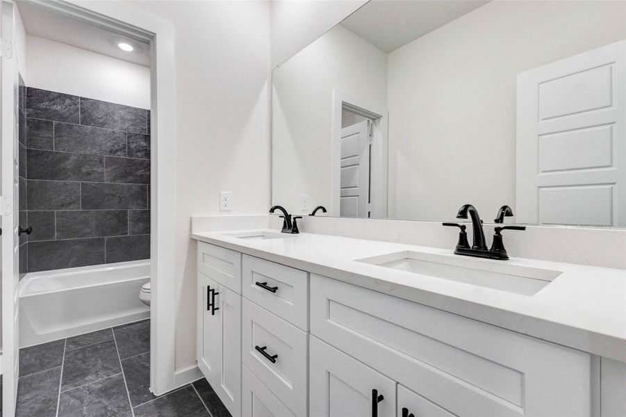 This stylish secondary bathroom features a double vanity with sleek quartz countertops and modern black fixtures, offering both functionality and elegance. The large mirror enhances brightness, while the adjoining tub and shower combination provides convenience for everyday use. Clean lines and contemporary finishes make this space both practical and inviting.