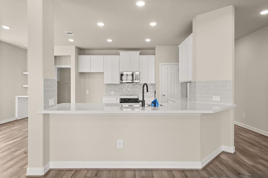 This light and bright kitchen features a large quartz island, white cabinets, a large sink overlooking your family room, recessed lighting, and beautiful backsplash.