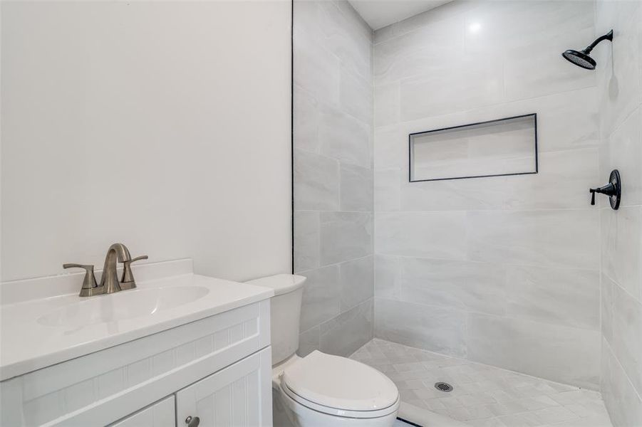 Bathroom featuring tiled shower, vanity, and toilet