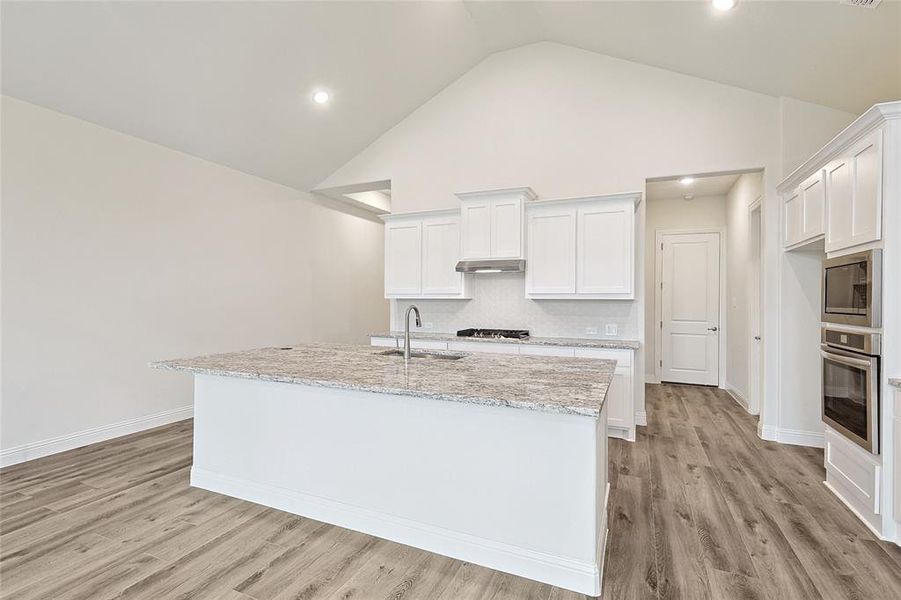 Kitchen featuring appliances with stainless steel finishes, light hardwood / wood-style floors, white cabinetry, light stone counters, and sink