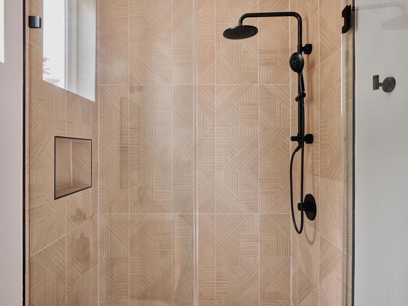 Shower enclosure featuring patterned tile walls, a built-in shower niche, and a matte black rainfall shower system with an adjustable handheld sprayer