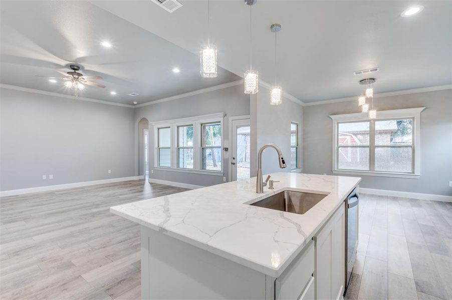 Kitchen with sink, white cabinetry, hanging light fixtures, an island with sink, and light stone countertops