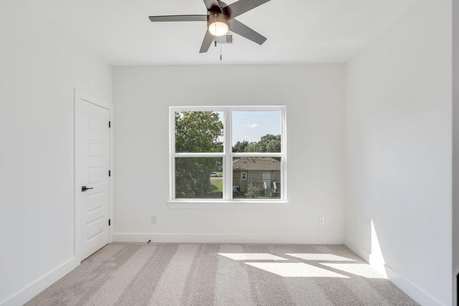 Secondary upstairs bedroom featuring plush carpet flooring, ceiling fan, and large window bringing in natural light.
