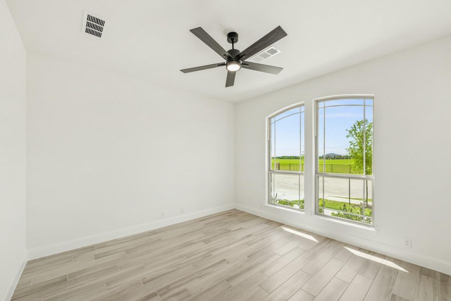 Empty room with light wood floors, ceiling fan, and arched windows overlooking a green yard Empty room with light wood floors, ceiling fan, and arched windows overlooking a green yard
