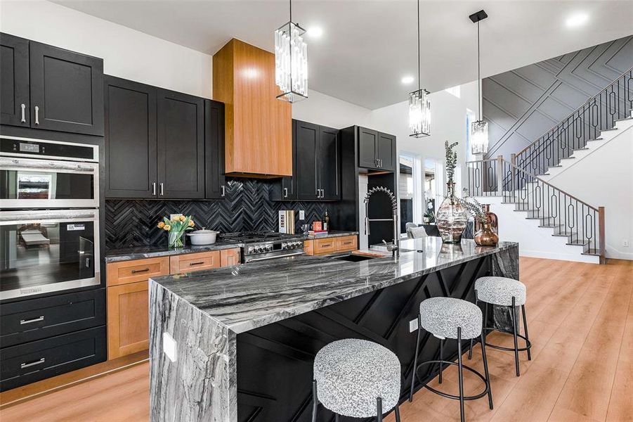 Kitchen featuring dark stone countertops, dark cabinetry, stainless steel appliances, a breakfast bar, and decorative light fixtures Kitchen featuring dark stone countertops, dark cabinetry, stainless steel appliances, a breakfast bar, and decorative light fixtures