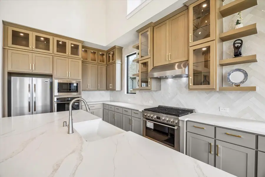 CHEF-INSPIRED KITCHEN INCLUDES CEILING-HEIGHT CABINETRY, GLASS-FRONT DISPLAY CABINETS, OPEN SHELVING, A LARGE GAS RANGE WITH STATEMENT VENT HOOD, QUARTZ SURFACES, AND A HERRINGBONE TILE BACKSPLASH. CHEF-INSPIRED KITCHEN INCLUDES CEILING-HEIGHT CABINETRY, GLASS-FRONT DISPLAY CABINETS, OPEN SHELVING, A LARGE GAS RANGE WITH STATEMENT VENT HOOD, QUARTZ SURFACES, AND A HERRINGBONE TILE BACKSPLASH.