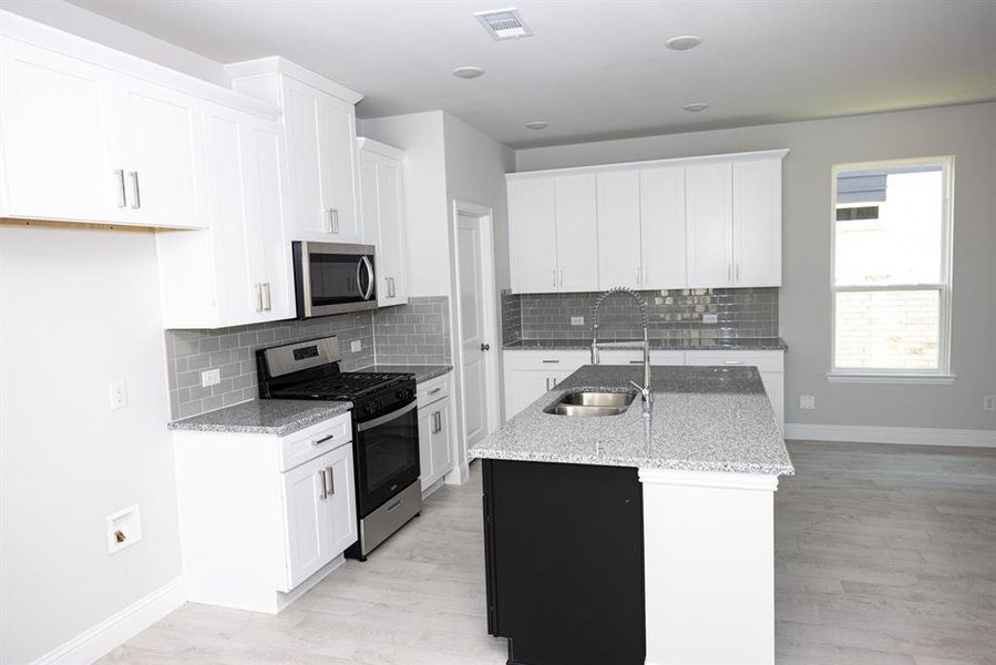 Kitchen featuring stainless steel appliances, a kitchen island with sink, backsplash, and light stone counters Kitchen featuring stainless steel appliances, a kitchen island with sink, backsplash, and light stone counters