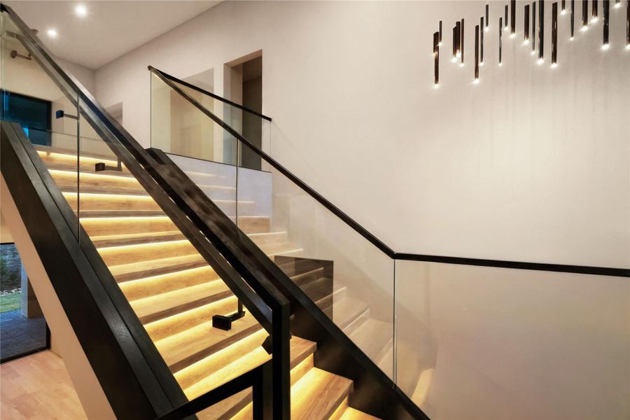 This modern staircase features sleek glass railings and warm under-step lighting, creating an elegant and inviting ambiance.