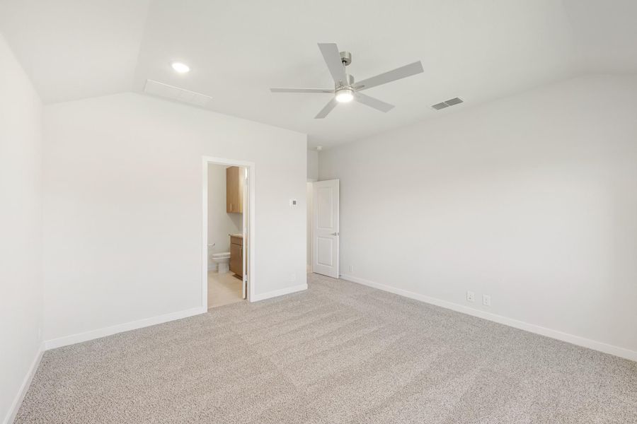 Empty bedroom with carpet, vaulted ceiling, ceiling fan, and ensuite bathroom doorway visible