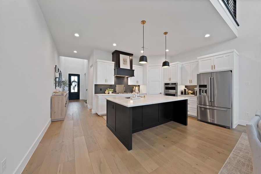 Spacious kitchen featuring a large black island, white shaker cabinetry, stainless steel appliances, and a black range hood Spacious kitchen featuring a large black island, white shaker cabinetry, stainless steel appliances, and a black range hood