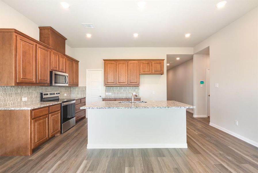 Kitchen featuring backsplash, a sink, appliances with stainless steel finishes, brown cabinetry, and wood finished floors