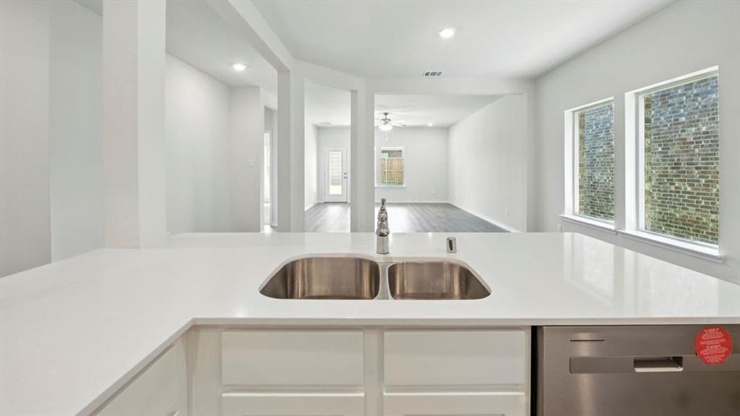 Kitchen featuring stainless steel dishwasher, white cabinets, open floor plan, recessed lighting, and light stone countertops Kitchen featuring stainless steel dishwasher, white cabinets, open floor plan, recessed lighting, and light stone countertops