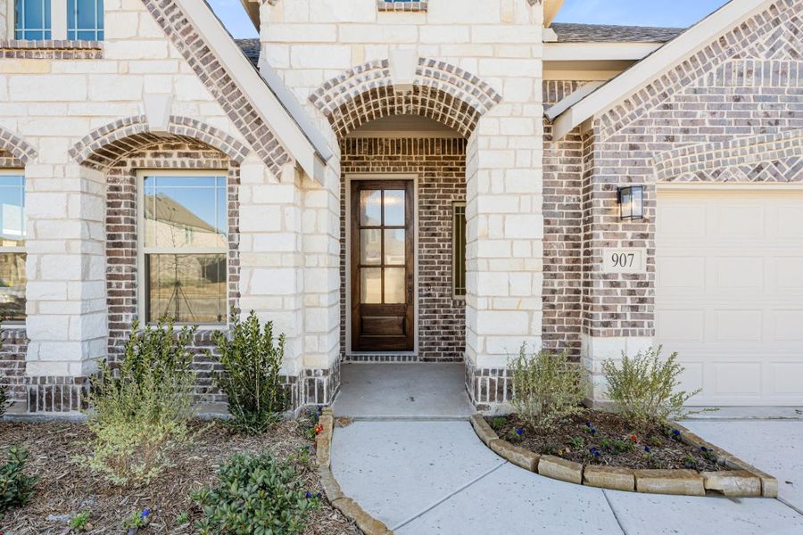Home entrance with stone and brick exterior, arched doorway, wood front door, and attached garage