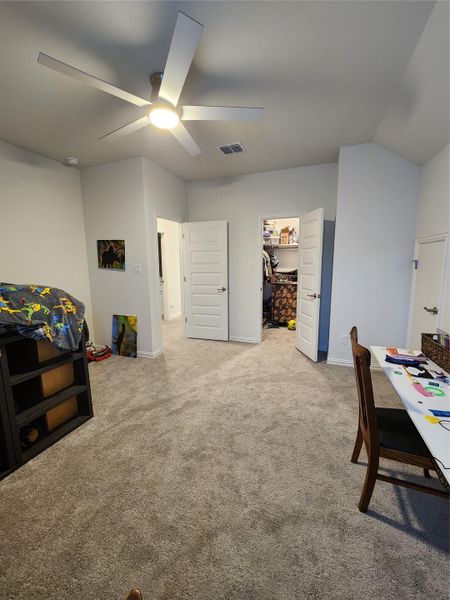 A comfortable bedroom with plush carpeting features an illuminating ceiling fan and accessible closet.