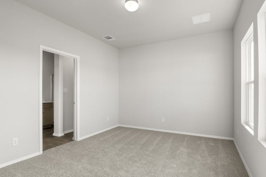 Image of primary bedroom with tan carpet and light grey walls with a connecting bathroom