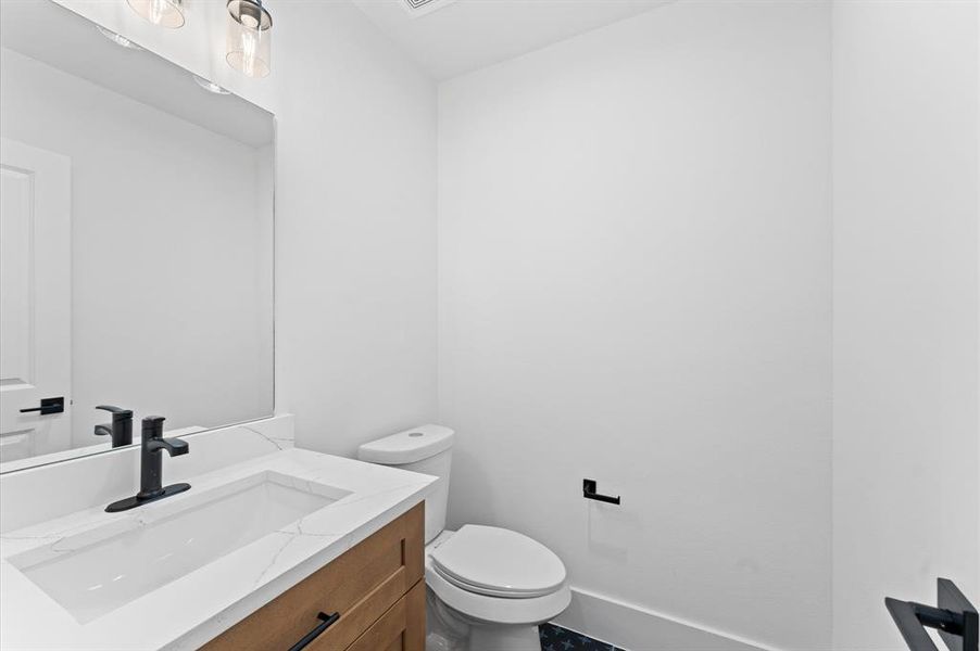 This is a modern, minimalist bathroom with a sleek white vanity, black fixtures, and a compact toilet. The neutral color palette and clean lines create a fresh, contemporary feel.