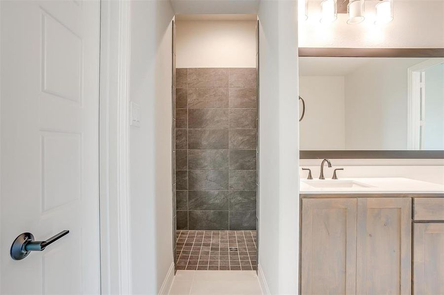 Bathroom with a tile shower, vanity, and tile patterned floors