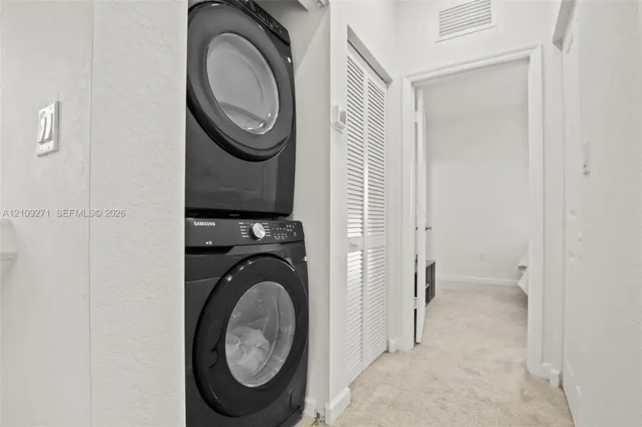 Laundry area featuring a stacked washer and dryer unit and louvered double-door closet cabinetry
