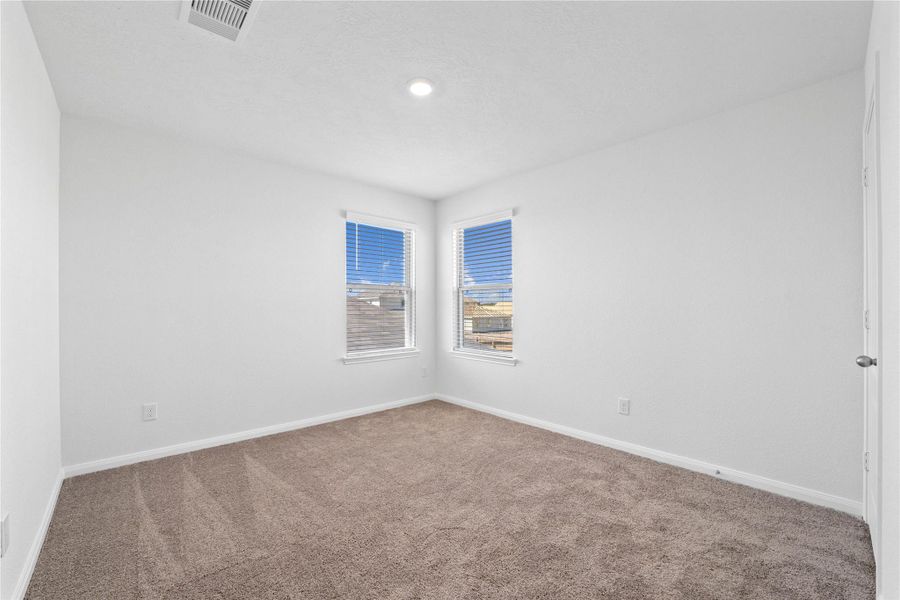 This secondary bedroom offers comfort and style with plush carpeting, neutral paint tones, recessed lighting, a large window with blinds, and a generously sized closet.