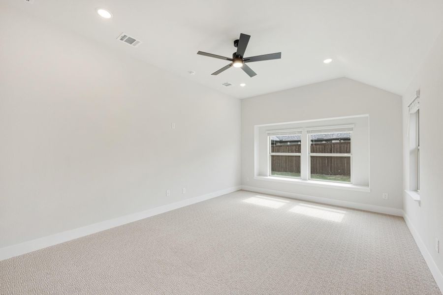 Empty bedroom with vaulted ceiling, ceiling fan, carpet flooring, and a large window