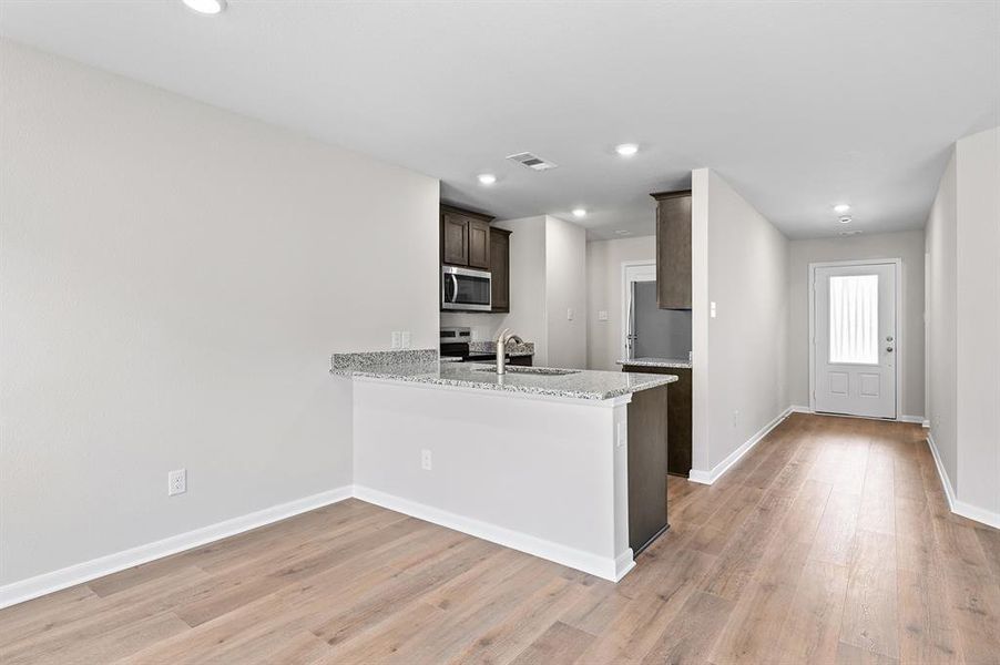 Kitchen featuring stainless steel appliances, light wood finished floors, dark brown cabinetry, a peninsula, and recessed lighting