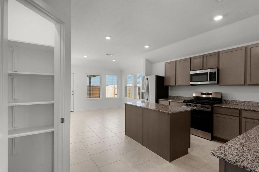 Kitchen featuring stainless steel appliances, a kitchen island, light stone counters, light tile patterned flooring, and recessed lighting