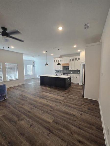 Kitchen featuring open floor plan, glass insert cabinets, hanging light fixtures, light countertops, and a kitchen island with sink