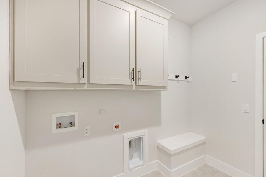 Laundry room with white upper cabinets, wall hooks, built-in bench, and washer and dryer hookups