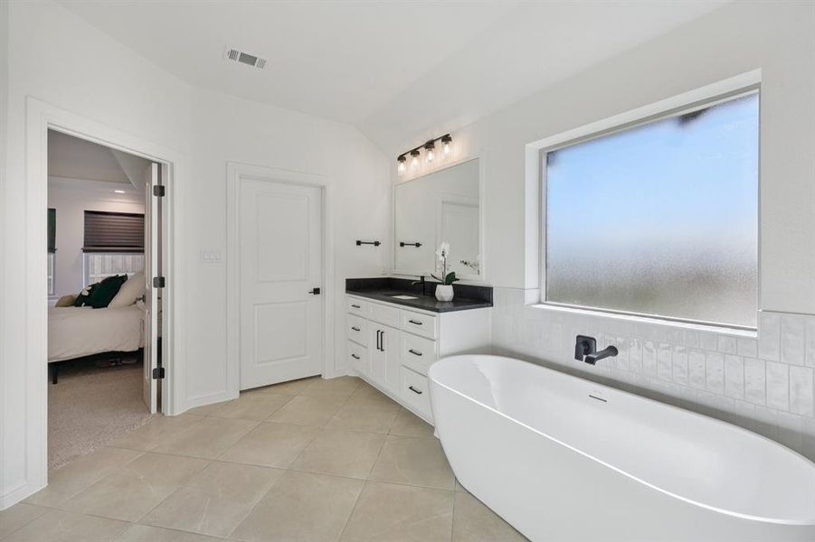 Full bathroom featuring a freestanding bath, vanity, connected bathroom, light tile patterned floors, and lofted ceiling Full bathroom featuring a freestanding bath, vanity, connected bathroom, light tile patterned floors, and lofted ceiling