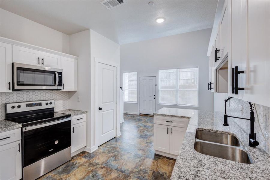 Kitchen featuring white cabinetry, light tile patterned floors, light stone counters, stainless steel appliances, and decorative backsplash