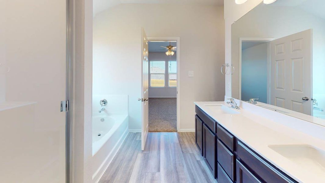 Bathroom with a garden tub, double vanity, light wood finished floors, ceiling fan, and lofted ceiling Bathroom with a garden tub, double vanity, light wood finished floors, ceiling fan, and lofted ceiling