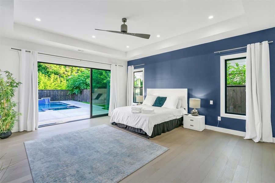 Bedroom featuring a raised ceiling, light wood-style flooring, access to outside, a ceiling fan, and recessed lighting