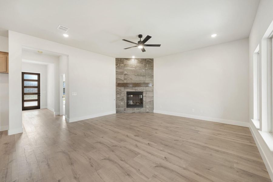 Open living room with light wood floors, stone tile fireplace, and ceiling fan