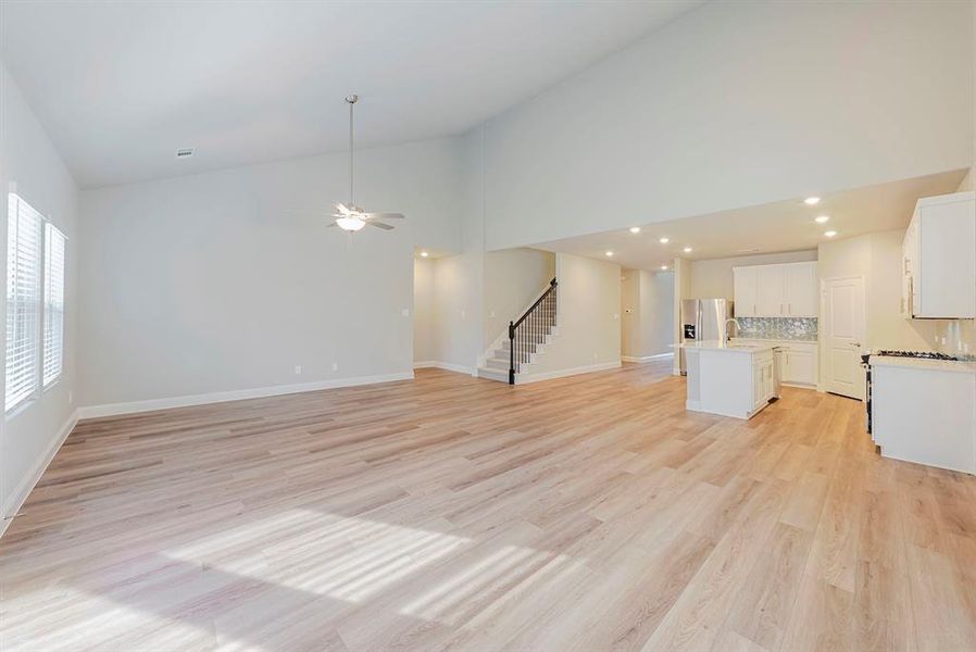 Unfurnished living room featuring light wood finished floors, high vaulted ceiling, stairway, and ceiling fan Unfurnished living room featuring light wood finished floors, high vaulted ceiling, stairway, and ceiling fan