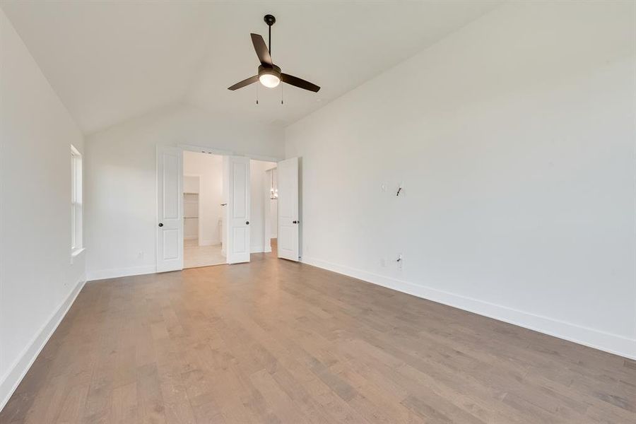 Unfurnished bedroom with lofted ceiling, wood finished floors, ceiling fan, and a walk in closet Unfurnished bedroom with lofted ceiling, wood finished floors, ceiling fan, and a walk in closet