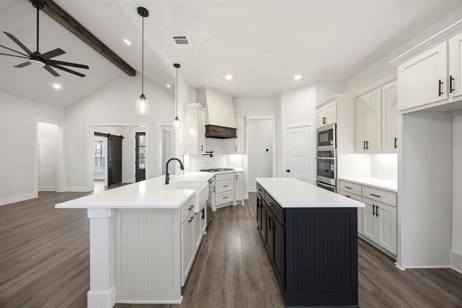 Kitchen featuring white cabinetry with dark hardware, dual islands, stainless steel double ovens and microwave, and wood-finish flooring