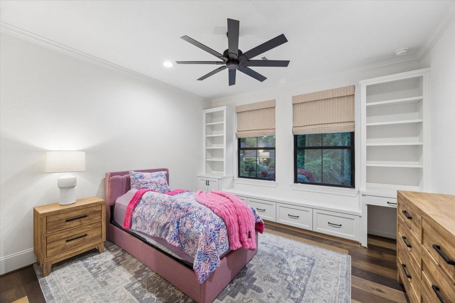 Comfort and craftsmanship define this inviting secondary bedroom. Custom carpenter-built shelving, integrated seating, and abundant natural light create a warm and highly functional retreat.
