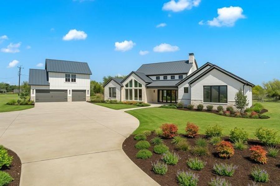 View of front facade with stone siding, a standing seam roof, driveway, a chimney, and a front lawn as per landscape plan