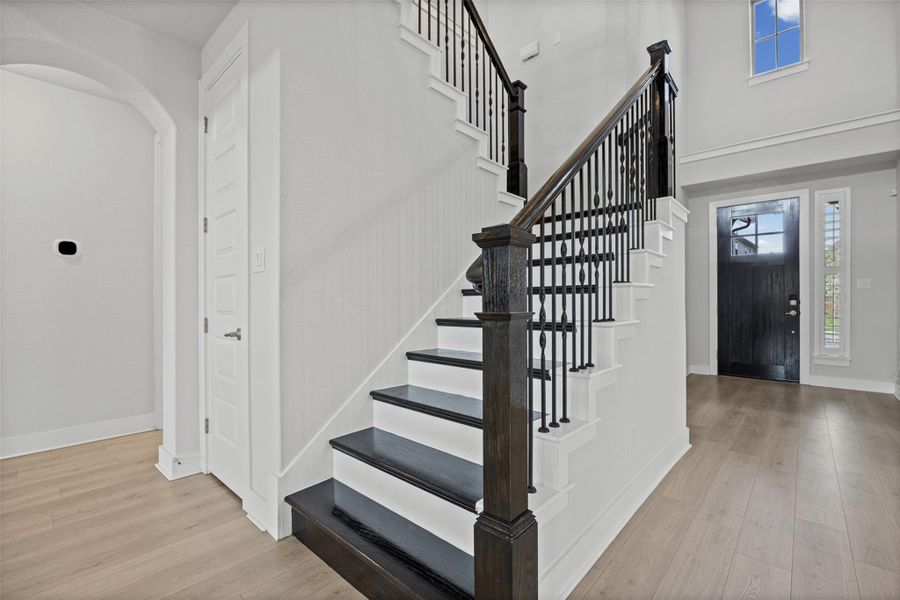 A grand entry unveils an elegant staircase with dark wood treads and wrought iron balusters, complemented by wide plank flooring.