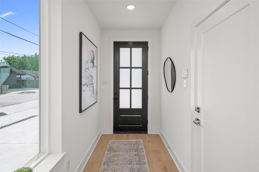 A sleek modern entry welcomes you home with warm white oak floors, clean architectural lines and a striking glass-paneled front door.