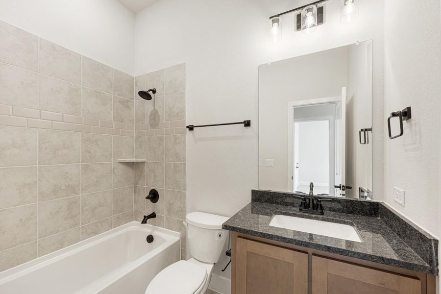 Bathroom with tiled tub-shower combo, dark granite vanity, wood cabinets, and black fixtures