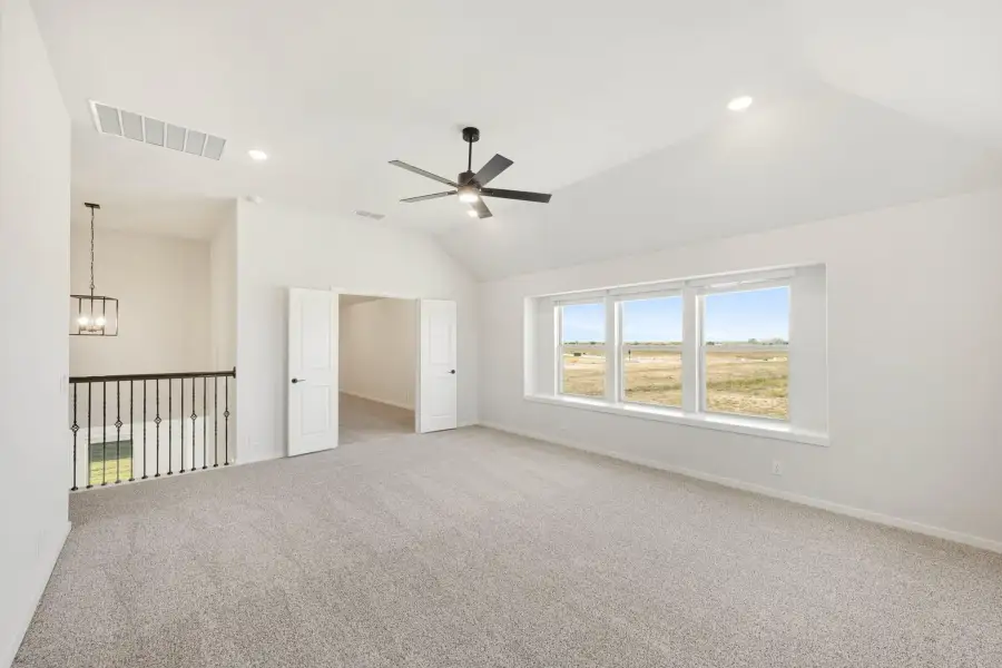 Spacious bedroom with vaulted ceiling, ceiling fan, carpet flooring, and large windows overlooking open land