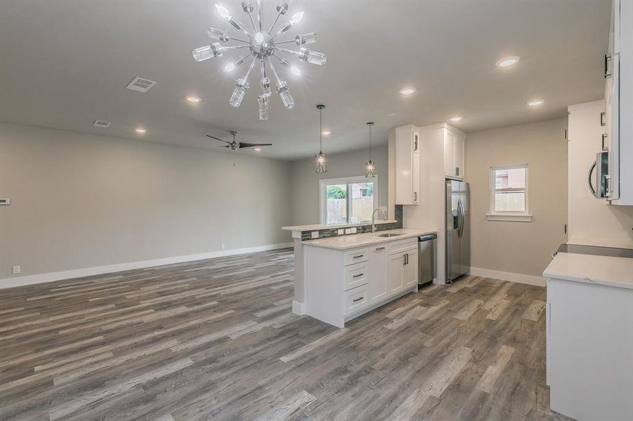 Kitchen with stainless steel appliances, hanging light fixtures, sink, hardwood / wood-style flooring, and white cabinetry