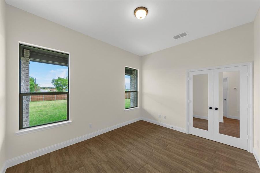 Room featuring wood-finish flooring, two large windows, white baseboards, and double French doors with black hardware