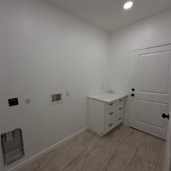 Laundry room featuring white cabinetry with black hardware, a light-toned countertop, and wood-finish tile flooring