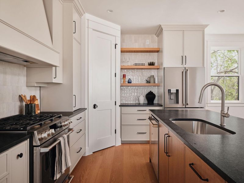 Kitchen with stainless steel appliances, open shelves, light wood finished floors, and backsplash