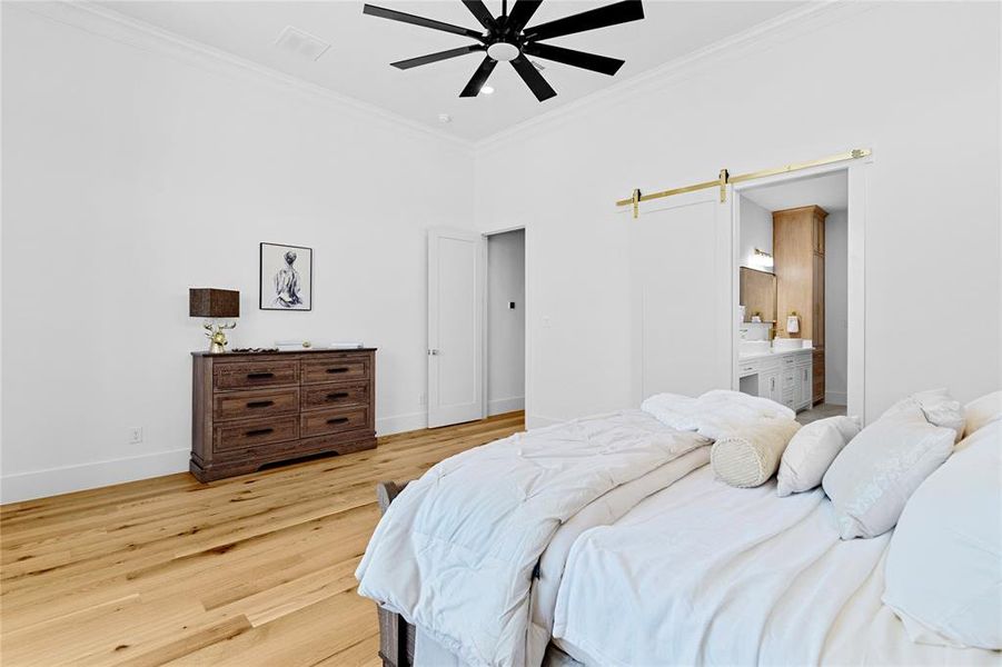 Bedroom with a barn door, crown molding, light wood-style floors, ceiling fan, and ensuite bathroom Bedroom with a barn door, crown molding, light wood-style floors, ceiling fan, and ensuite bathroom