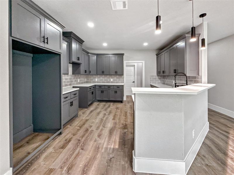 Kitchen with gray cabinetry, decorative backsplash, a peninsula, pendant lighting, and light wood finished floors
