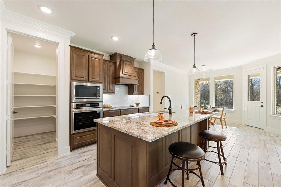 Kitchen featuring decorative light fixtures, light stone countertops, light wood-type flooring, appliances with stainless steel finishes, and ornamental molding