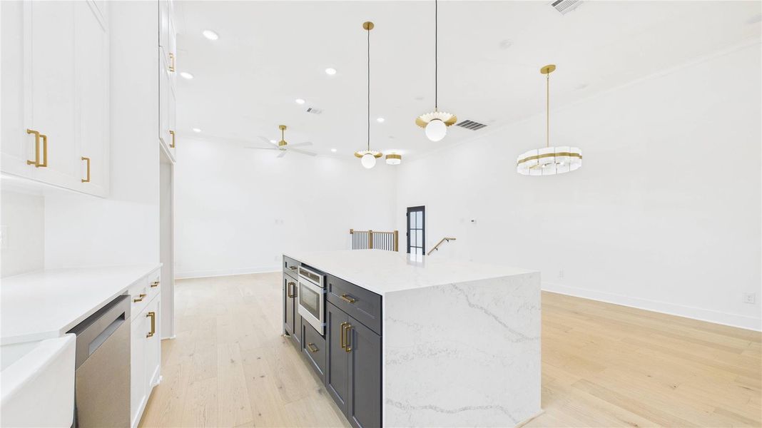 Sleek pendant lighting. High ceilings and waterfall quartz countered island enhance the spacious feel.